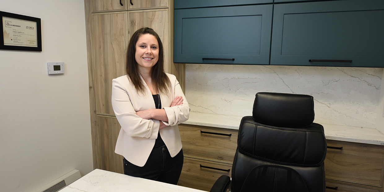 Smiling woman with her arms crossed standing before natural wood and dark blue cabinets