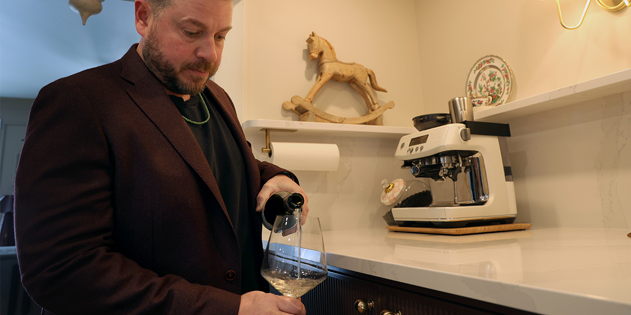 Man wearing a suit and serving wine next to a home bar with a white countertop and black cabinets